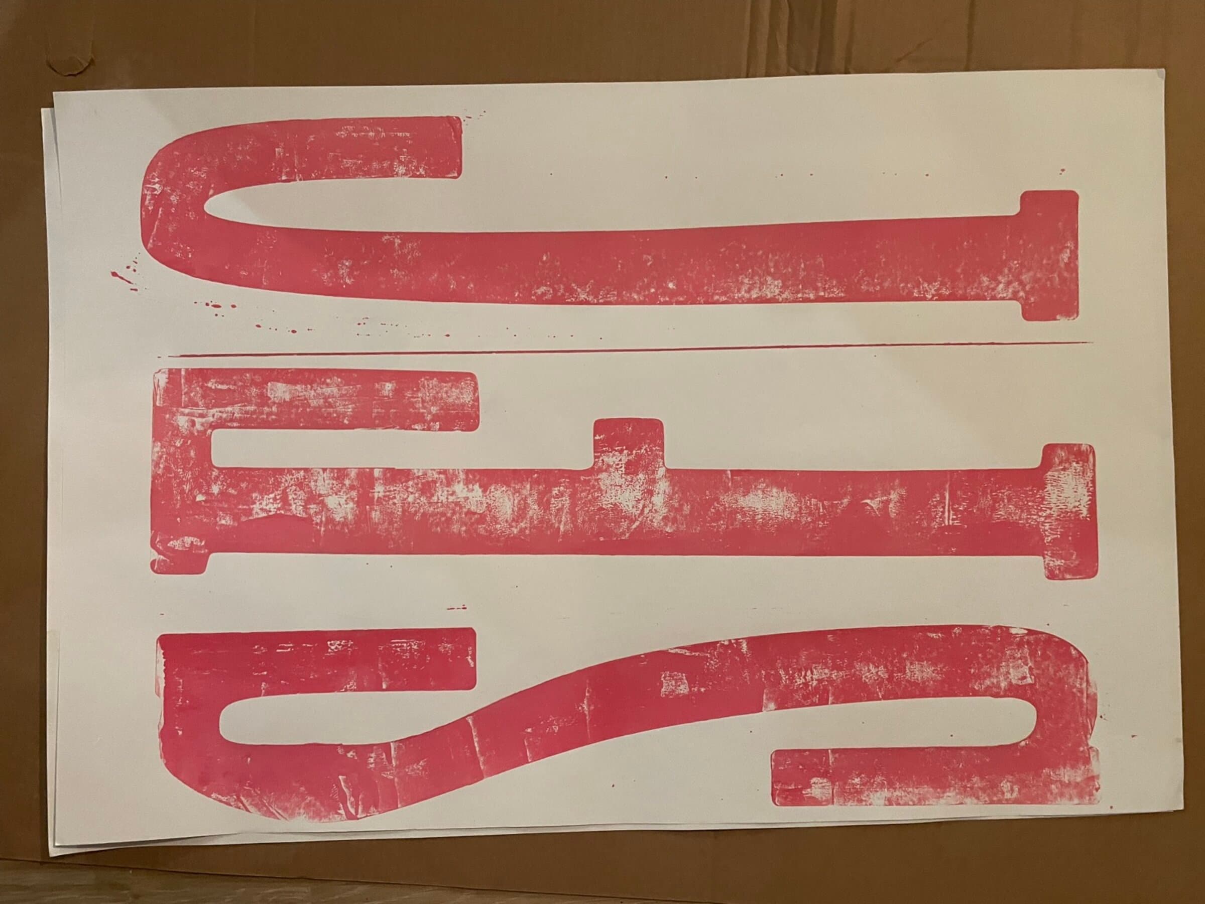 A third pull of three giant carved letters (reading roughly S, T, T) in pink across a horizontal white sheet on cardboard. Heavy distressed ink coverage, hand-pressed unevenness visible throughout.