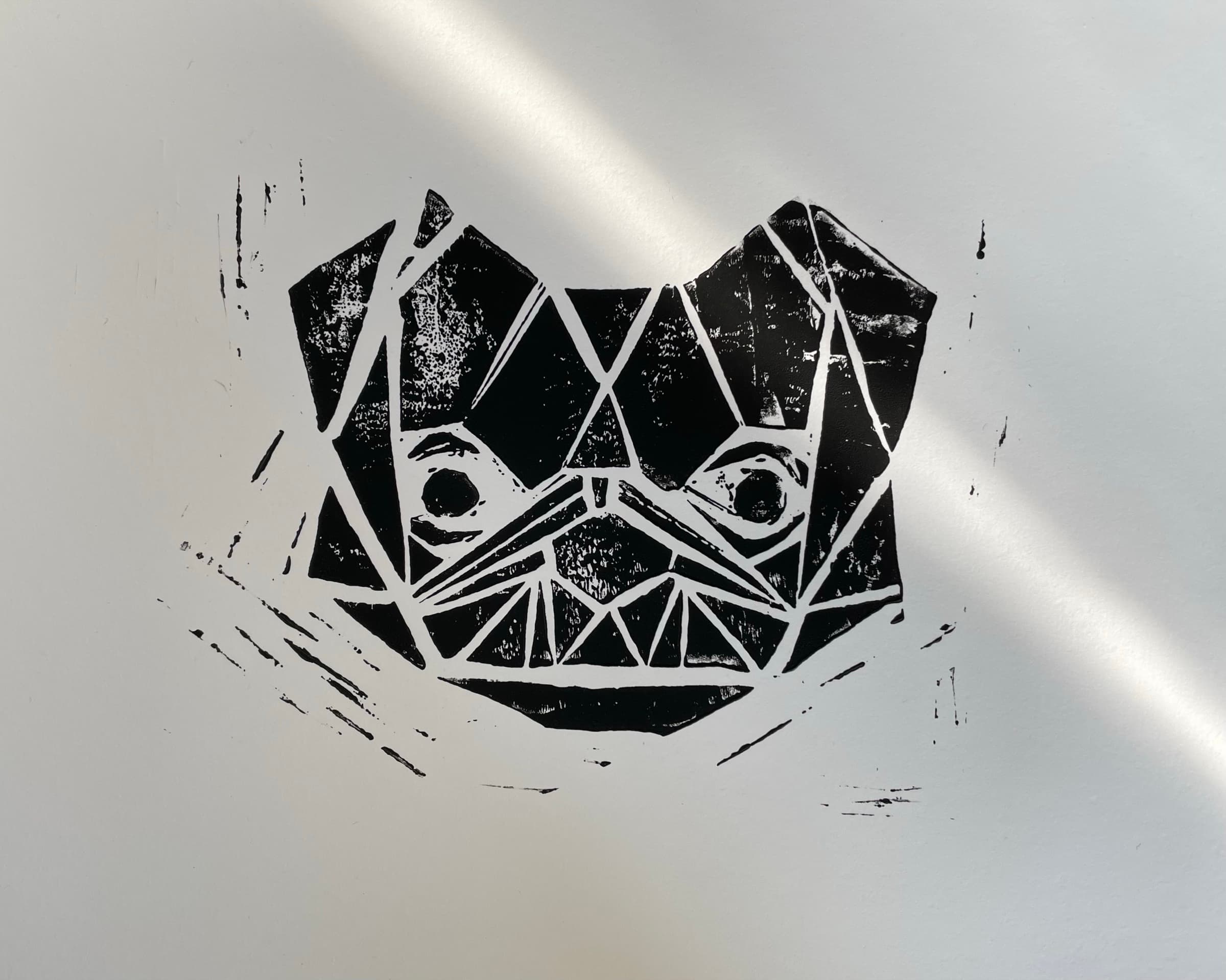 A graphic linoleum-cut print of the bulldog face on cream paper: solid black for the masses with hand-cut white slivers between the planes. Soft natural light rakes across the surface from upper right.