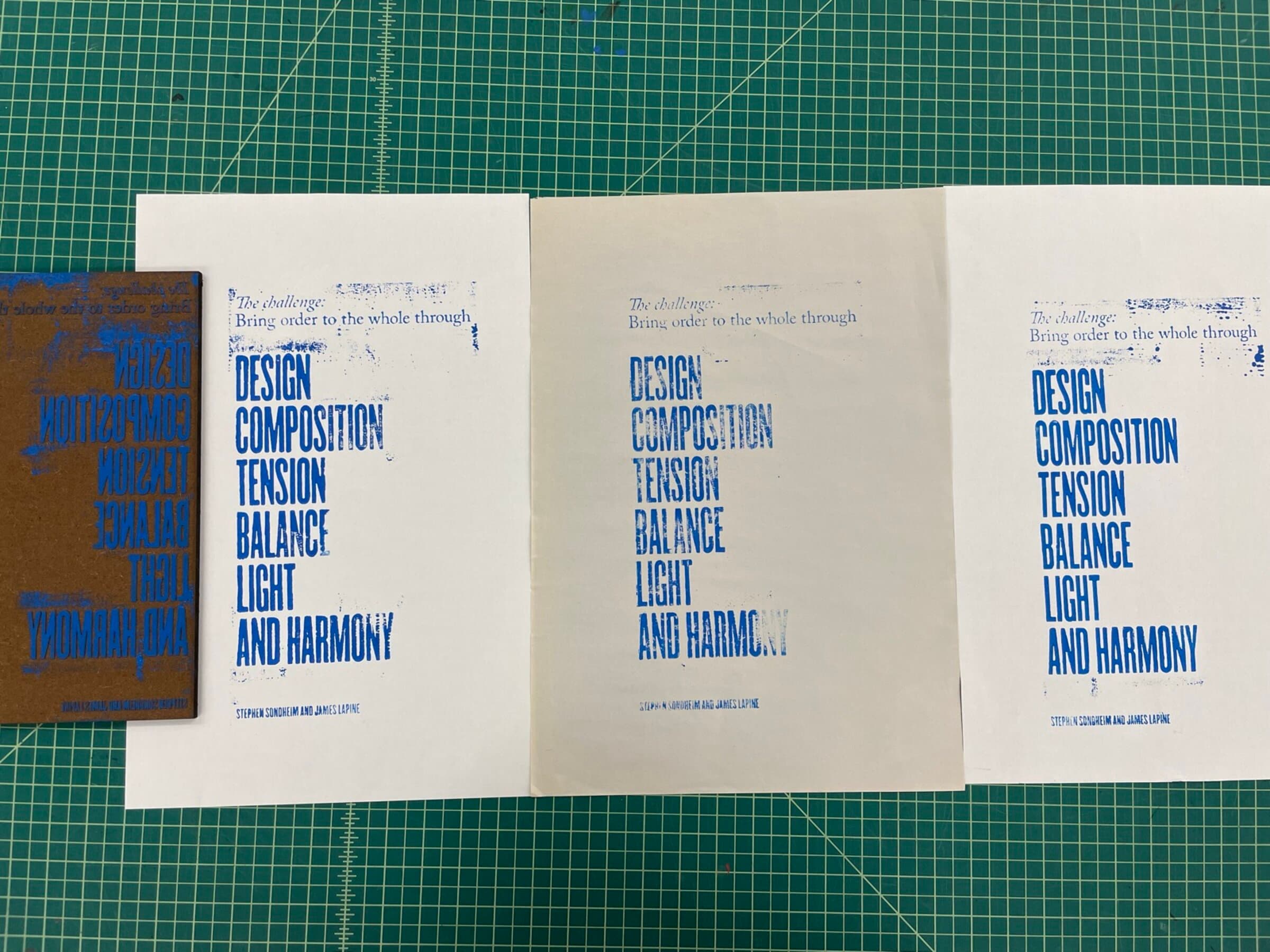 A studio flat-lay on a green cutting mat: three white sheets in a row, each pulled with the same Sondheim quote in cobalt-blue ink. The quote runs 'The challenge: Bring order to the whole through' set in italic above DESIGN COMPOSITION TENSION BALANCE LIGHT AND HARMONY in chunky stacked sans caps, attribution 'Stephen Sondheim and James Lapine' set tight at the bottom. To the left of the three pulls sits the inked basswood block itself, mirrored and unread.