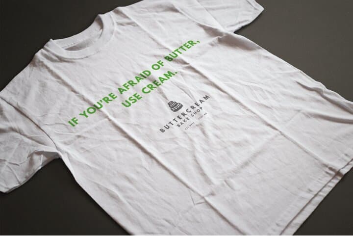 A white t-shirt printed with IF YOU'RE AFRAID OF BUTTER, USE CREAM set in two stacked lines of green caps wrapping under the Buttercream badge mark.