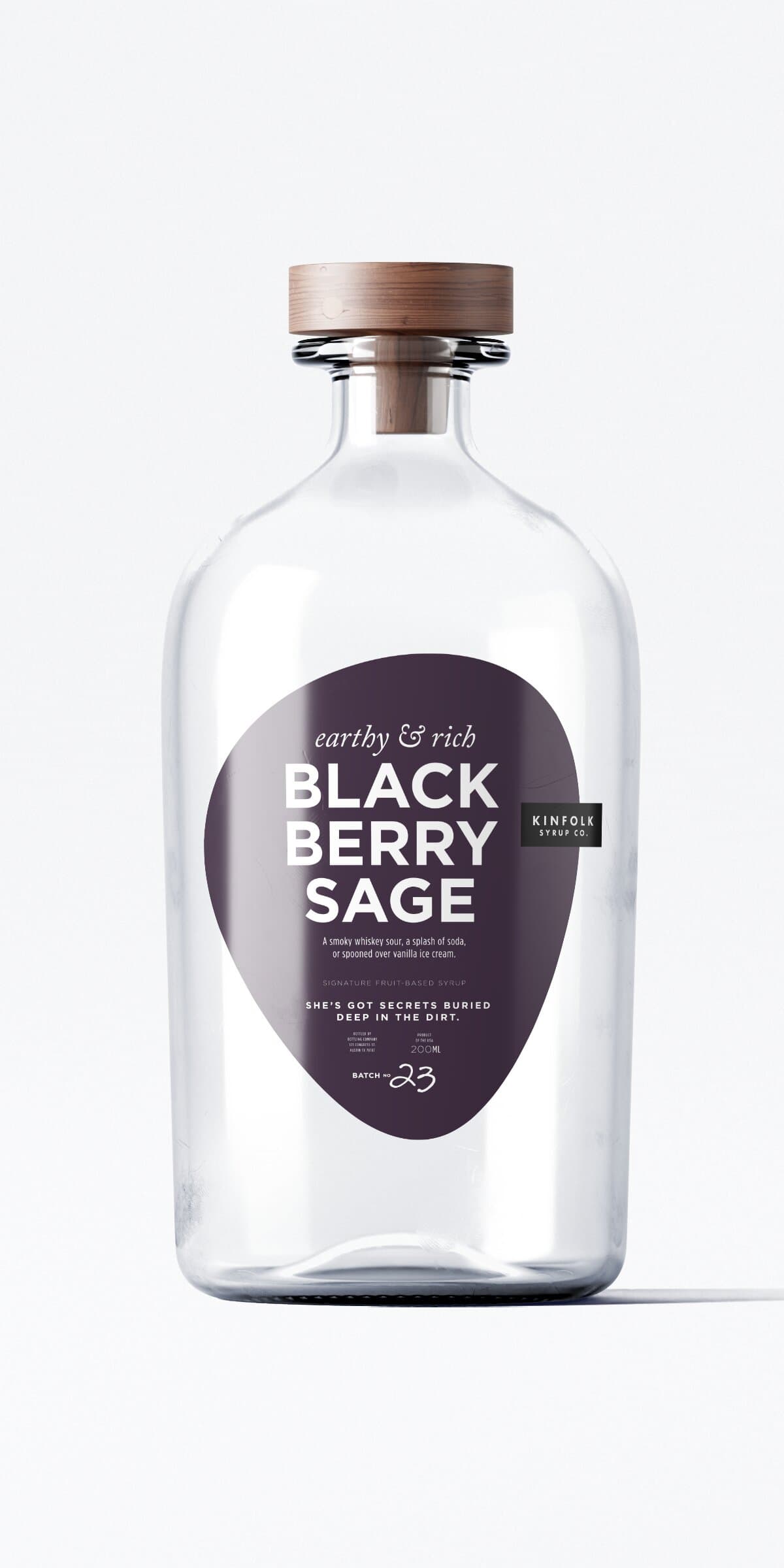 The Blackberry Sage bottle: same apothecary glass and wooden cap, deep wine-purple teardrop label with the wordmark tag in the right shoulder of the teardrop.