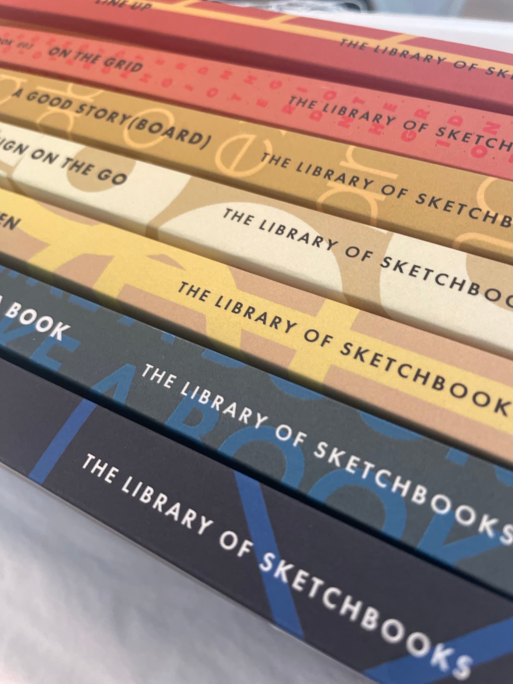 A tighter detail of three spines showing the consistent brand-mark band running across each one, with three different individual title and pattern treatments visible underneath the band.